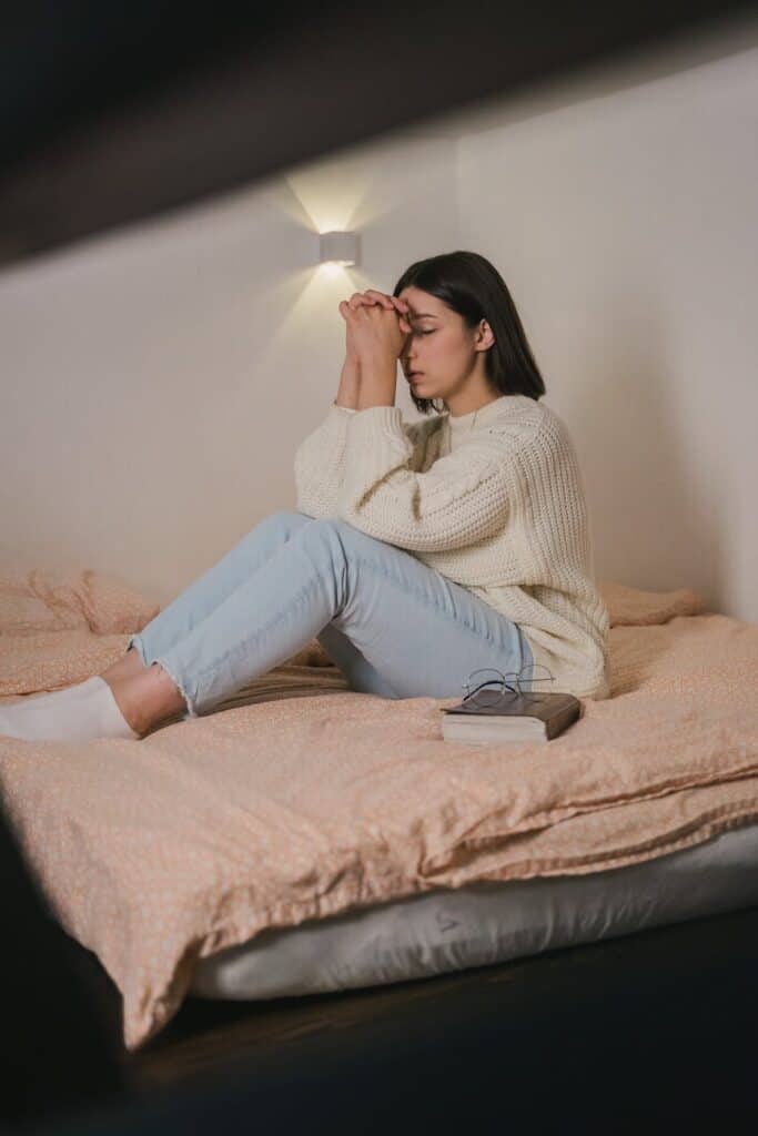 woman in white sweater and blue denim jeans praying on bed, fertility prayer