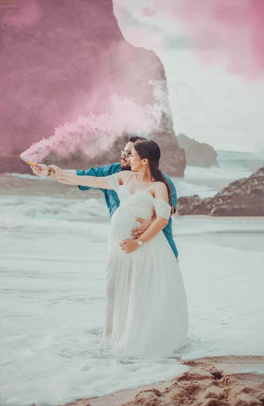 man and a woman on shore holding a pink smoke bomb