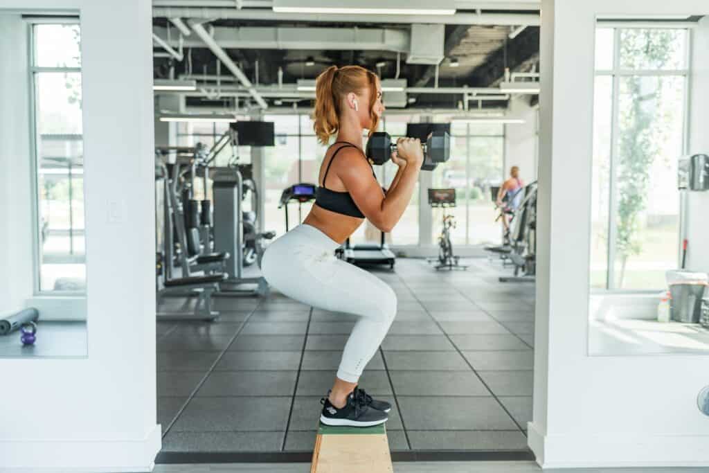 woman wearing black sports bra and white legging lifting dummbells